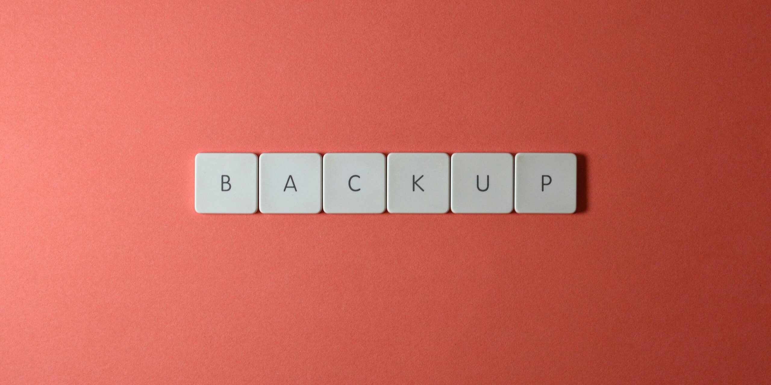 Free Close-up of keyboard keys spelling 'BACKUP' placed on a coral-colored surface. Stock Photo