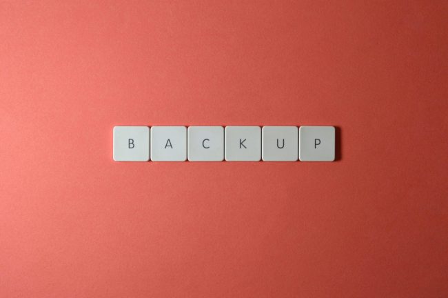 Free Close-up of keyboard keys spelling 'BACKUP' placed on a coral-colored surface. Stock Photo
